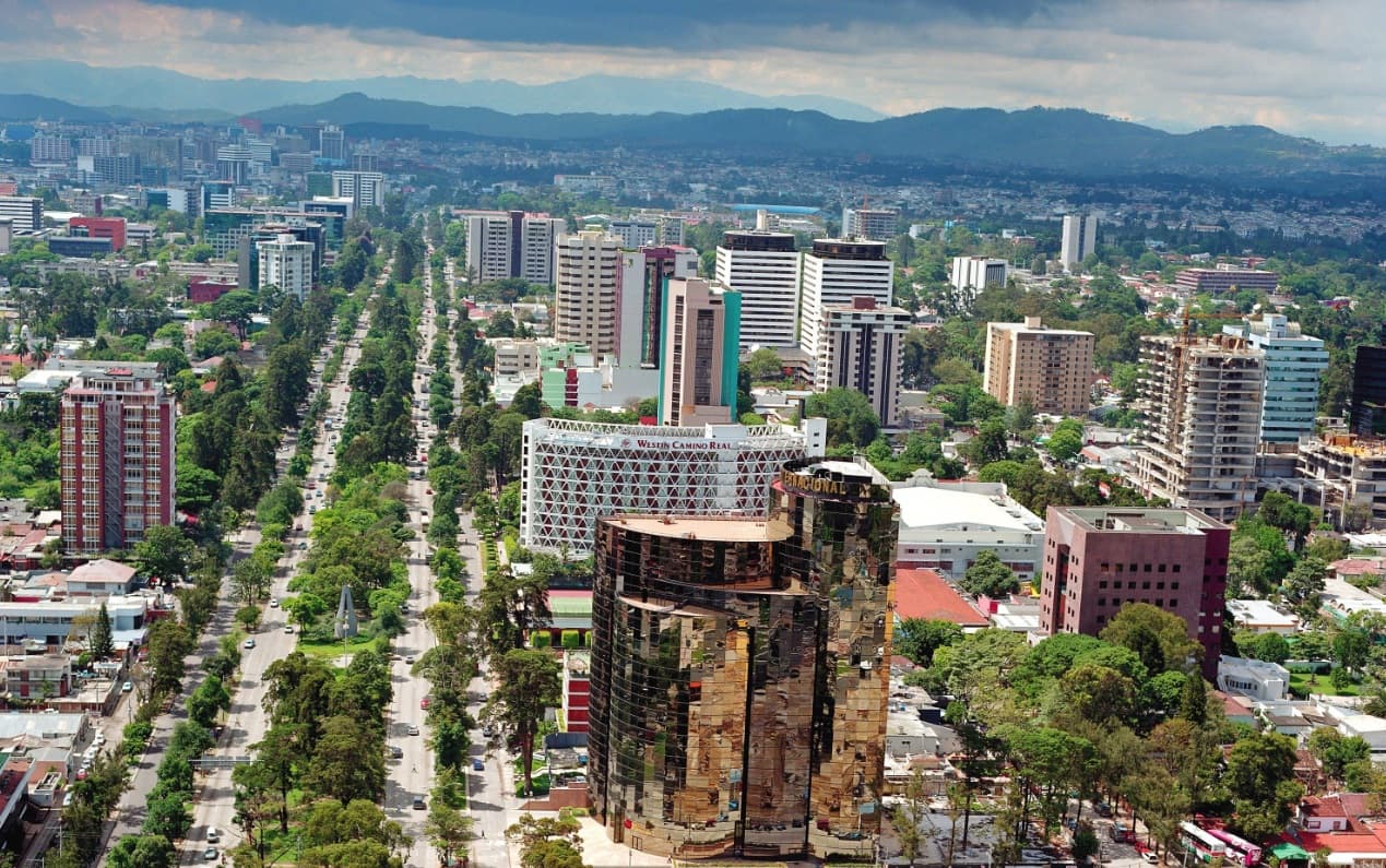 Avenida La Reforma seen from the air: the tree-lined boulevard running through Guatemala City, with the sierra closing the horizon.
